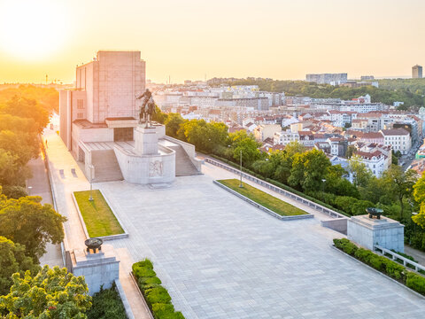 Sunrise casts light on the National Monument at Vitkov in Prague. The tomb of the Unknown Soldier stands at the center, surrounded by buildings and trees. This moment captures the city awakening.