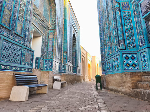 Shah-i-Zinda necropolis alley in Samarkand with ornate blue tilework on mausoleum facades. Empty pathway between decorated buildings ideal for travel and heritage publications.