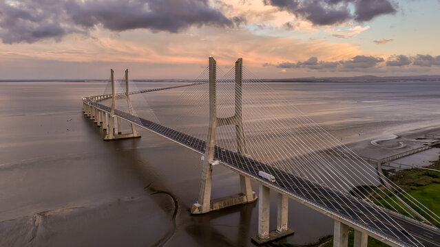 Aerial view of the Vasco da Gama Bridge spanning the Tagus River under a dramatic sunset sky with soft clouds Lisboa, Portugal.