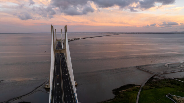 Aerial view of Vasco da Gama Bridge stretching across the Tagus River under a dramatic sunset sky with soft clouds Lisboa, Portugal.