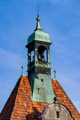 Plakat Old church bell tower with green copper roof and tiles. Historic bell tower steeple with weathered green copper patina and orange roof tiles against blue sky. European architecture and travel concept