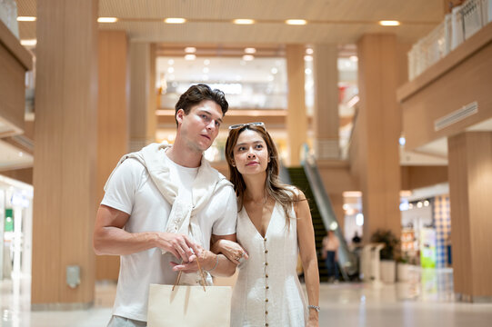 Asian woman girlfriend linking arms with white man boyfriend while walking together in shopping mall