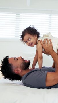 Father, lift and play with baby girl on bed with smile, bonding and connection with love, laugh and care. People, dad and child for flight, relax or fun with toddler for plane game in family home