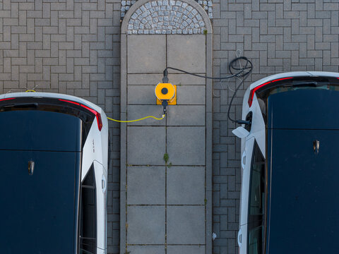 Aerial view of two electric cars plugged into the yellow ENTEGA Charging Station on a paved parking lot in Darmstadt, Hessen, Germany.