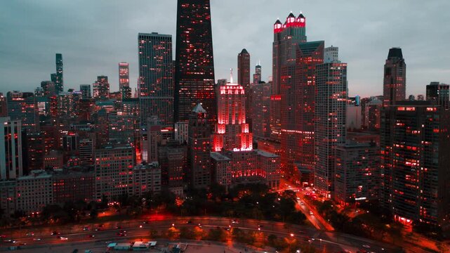 A cinematic hyperlapse of downtown Chicago at dusk, capturing the city skyline as glowing lights begin to illuminate the skyscrapers beneath a dramatic cloudy sky. This moody aerial view highlights th