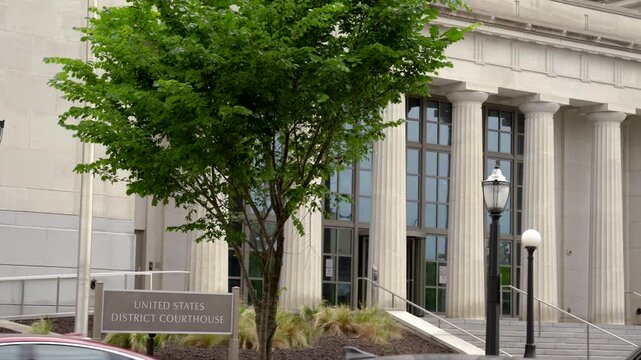 A panning shot captures the United States District Courthouse in Mobile, Alabama, featuring grand white columns, landscaped greenery, parked vehicles, and stately civic architecture.