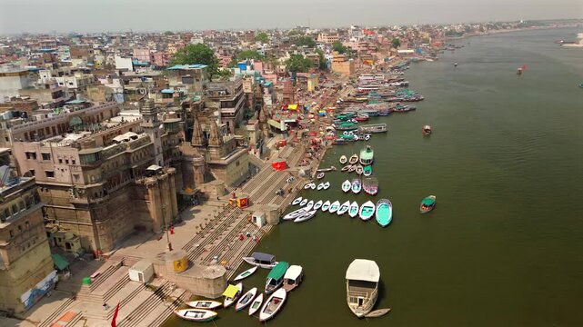An aerial wide static shot displaying the historic stone ghats, traditional palaces, and rows of colorful tourist boats docked along the sacred Ganges River in Varanasi, India