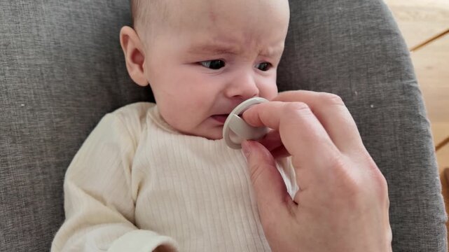 Close-up of a cute newborn child rejecting a dummy binky by spitting it out. Concept of baby moods, childhood, and infant care lifestyle.
