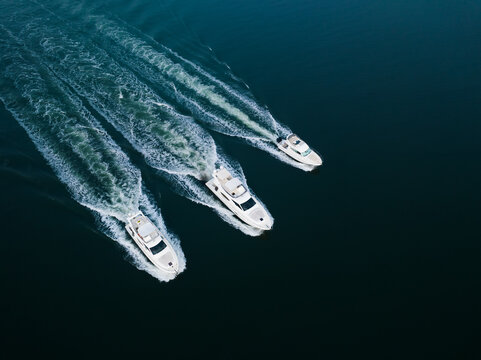 Aerial view of three white yachts cruising in parallel across deep blue water with prominent white wakes in Panaji, Goa, India.