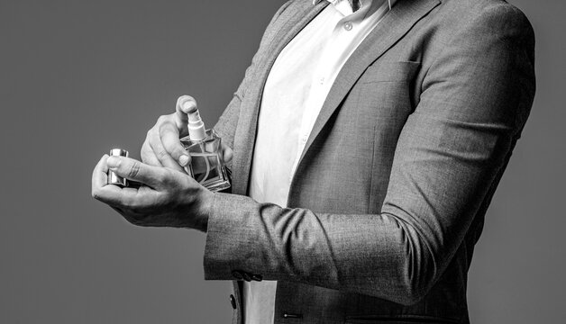 Bottle of perfume. Men perfume in the hand on suit background. Handsome man in formal suit and with bottle of perfume, closeup. Black and white