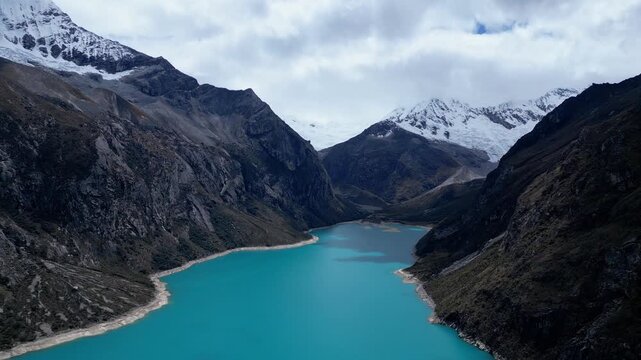 Huaraz, Peru: Forward footage of famous laguna paron in Caraz, Huaraz region, Peru. Surrounded by mountain range and with cloudy dramatic sky, showing cordillera blanca in the background