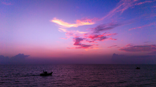 Aerial view of fishing boats sailing on the calm sea under a purple and pink sunset sky in South Goa, Goa, India.