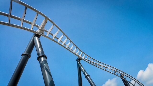 An empty roller coaster track curving sharply downwards against a blue sky.