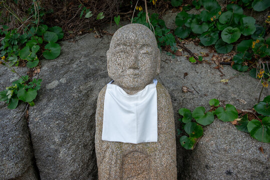 Traditional Japanese Jizo Stone Statue with White Bib Among Rocks and Green Vegetation