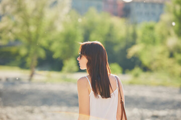 Fototapeta premium Woman, tourist and sightseeing with sunglasses in nature for outdoor vacation or summer holiday. Profile, female person or traveler walking with sunshine in garden or park for travel or destination