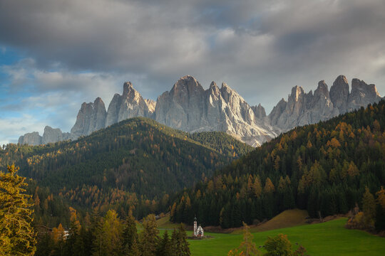 The iconic St Johann Church in Ranui on a green meadow below the Odle mountain peaks in autumn. Santa Maddalena, South Tyrol, Italy.