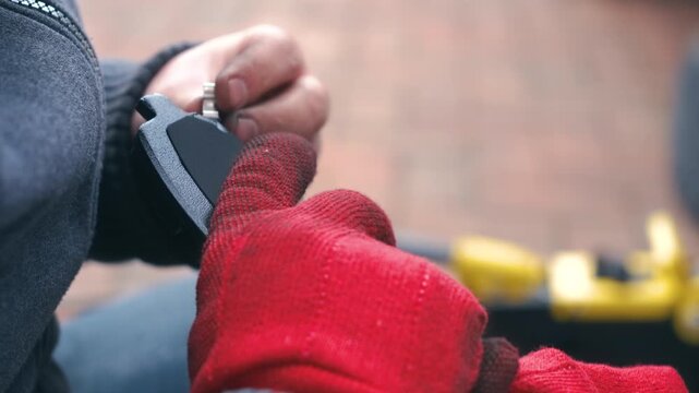 Technician installing mechanical wear indicator on brake pad during car repair. Close up automotive replacement process with hands fitting metal clip onto friction pad component. Vehicle brake