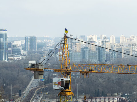 Kyiv, Ukraine - March 21, 2026: A yellow Liebherr tower crane stands at a construction site with the Ukrainian flag above, representing urban development and modern infrastructure