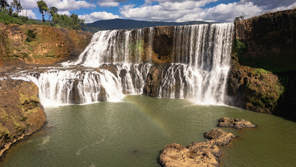Aerial drone view of Sae Pong Lai Waterfall in Sekong Province, southern Laos. The powerful wide waterfall cascades over multiple rocky tiers into a large green pool below, surrounded by dense tropica © jr