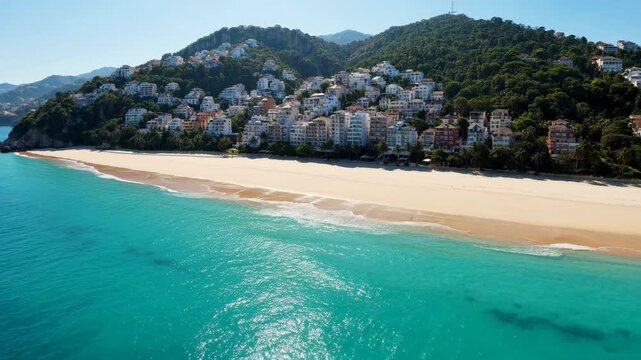 Beautiful sandy beach with turquoise sea water and houses on the green mountain slope in a sunny summer day 4K video