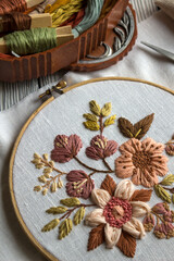 Fototapeta premium Elegant floral embroidery composition in warm brown tones stretched in embroidery hoop with sewing tools nearby. Cozy handmade needlework scene with embroidery supplies and copy space for craft design
