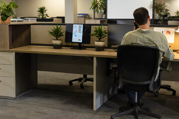 Mature man sitting in ergonomic chair at open office holding phone two monitors chart, copy space © wavebreak3