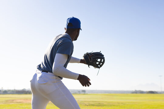 Baseball player is fielding with leather glove on outfield grass under clear blue sky