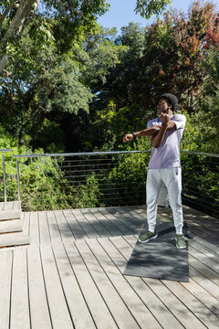 African American man standing stretching arms across chest on deck mat by cable railing, copy space