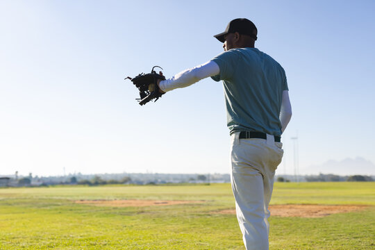Baseball player is extending left arm with dark leather glove on grassy field near city