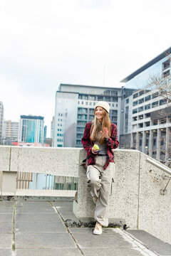 Woman is leaning on low concrete parapet holding green apple and gesturing on urban terrace