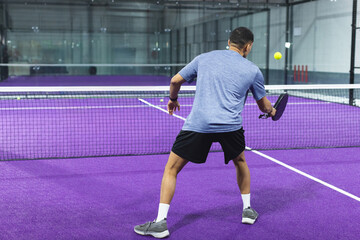 Obraz premium Blue-shirted man holding black paddle near net preparing to strike yellow ball on purple court