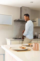 African American man holding spatula cooking on cooktop with frying pan in kitchen, copy space © wavebreak3