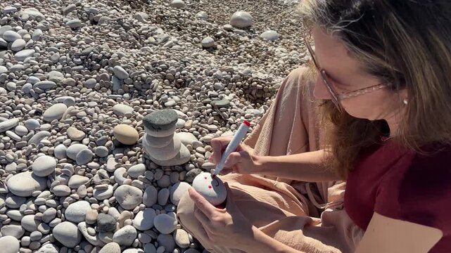 Mujer dibujando sonrisa en piedra junto al mar