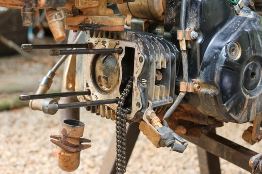 Abandoned motorcycle engine undergoing extensive mechanic repair with disassembled broken rusty cylinder block and hanging chain showing neglected state of heavy machinery