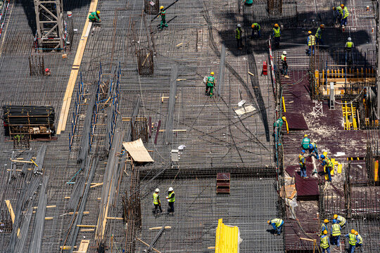 Aerial view of construction workers installing steel rebar reinforcement on a large building foundation site with various materials and equipment Dubai, Dubai, United Arab Emirates.
