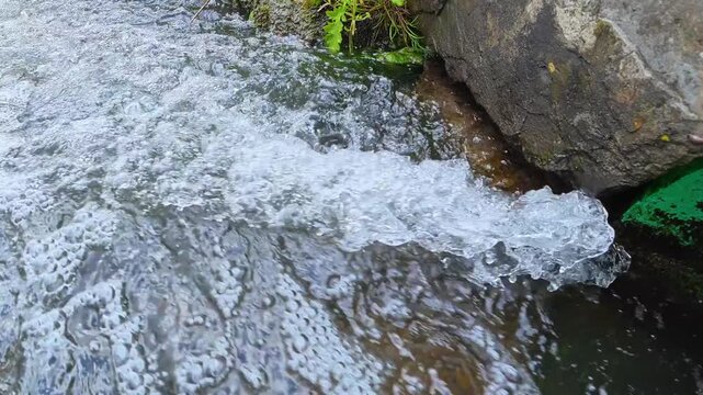 Crystal clear stream water flowing forcefully from a drainpipe creating bubbles and foam