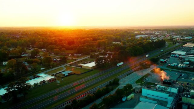 Cinematic golden hour drone aerial of a white semi-truck hauling freight on a divided suburban highway in Mauldin, South Carolina, with warm orange sky and residential landscape below.