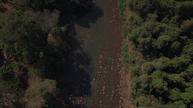 Aerial shot flying backward above the river before tilting up to reveal Pha Suam Falls, with rocky rapids, forest and flowing water in Laos.