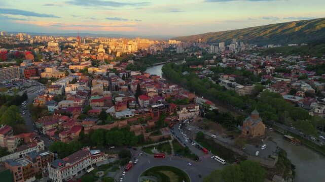 Drobe fly above Tbilisi city skyline at sunset, aerial of the capital of Georgia during golden hours with old town