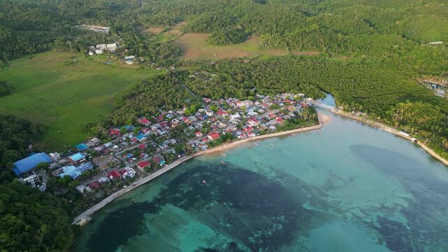 Vibrant aerial orbit of coastal village barangay amid lush tropical island greenery and shallow reefs - Magnesia Del Norte, Catanduanes, Philippines