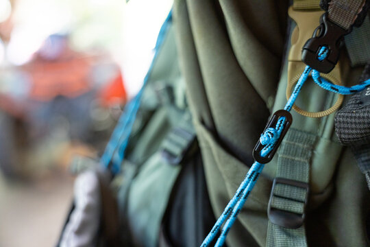 Close up of an olive green tactical outdoor backpack with bright blue rope tied in secure knot to plastic buckle expressing prepared and rugged sense of exciting adventure and readiness