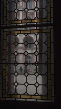 Interior view through a stained glass window overlooking the courtyard of a castle, with geometric leaded glass patterns and soft architectural blur outside.