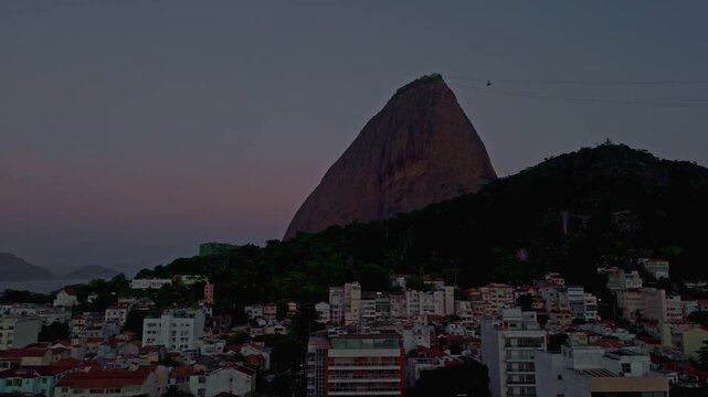 Aerial drone shot of the iconic Sugarloaf Mountain and cable cars at dusk in Rio de Janeiro, Brazil. View of the Urca neighborhood buildings.