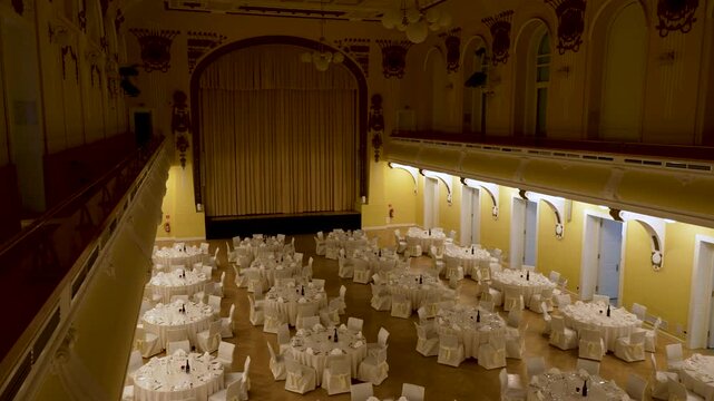 Elegant banquet setup inside Grand Hotel Union Hall in Ljubljana, with round white-clothed tables, ornate balconies, and a grand stage in a historic event venue.