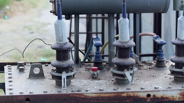 Close-up of old corroded electric transformer with ceramic insulators and wiring in rural setting. Ideal for power infrastructure, energy crisis, and development documentaries.