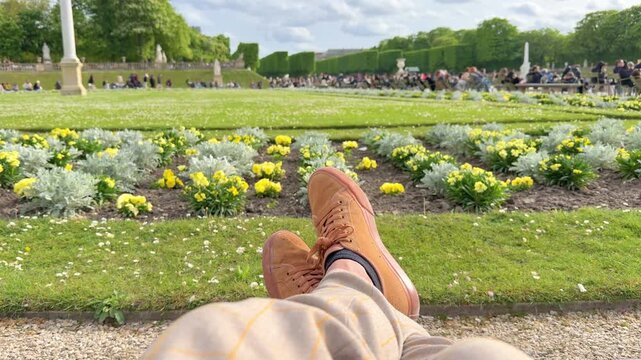 POV Point of view of relaxed person sitting and enjoying the view of the beautiful flowerbeds and lawn at the Jardin du Luxembourg in Paris on a sunny spring day, with other tourists in the background