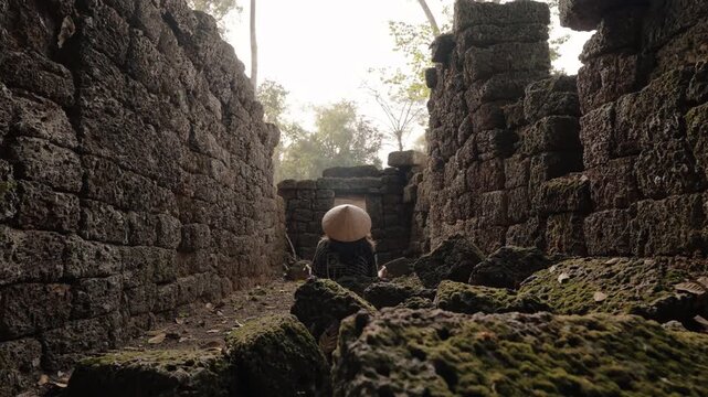 Traveler wearing conical hat exploring ancient stone ruins in Siem Reap Cambodia