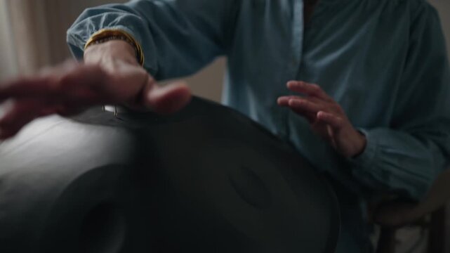 Slow motion medium shot of a person playing a handpan during a calm indoor music session.