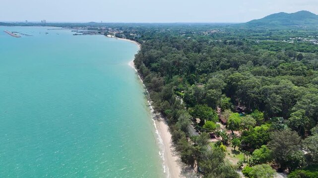 Drone footage aerial view of beautiful tropical beach coastline with turquoise sea water, white sand, and dense green tree forest