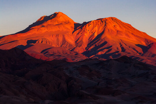 Aerial view of majestic mountain peaks glowing in the warm light of sunset over the arid desert landscape Toconao, Antofagasta, Chile.